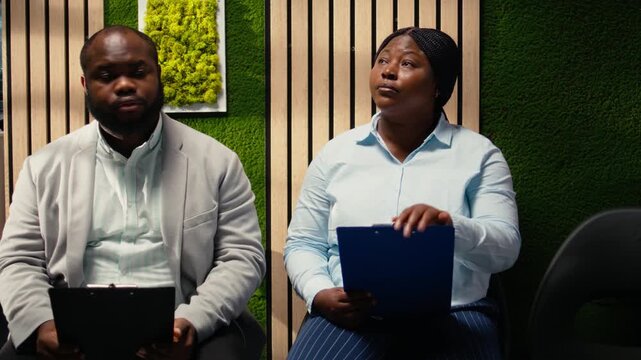 Anxious black woman job seeker getting called in the HR office to start interview, awaiting discussion and showcasing anticipation in office. People preparing for the recruitment process. Camera A.