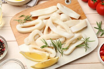 Uncooked squid rings, spices and tomatoes on wooden table, flat lay