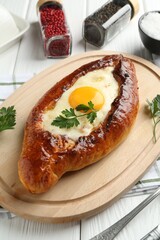 Tasty khachapuri with cheese, egg and spices on white wooden table