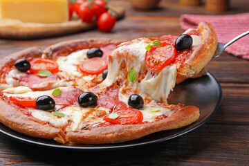 Taking piece of delicious pizza with cheese, salami, tomatoes and olives at wooden table, closeup