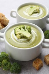 Tasty broccoli cream soup served with croutons on light grey table, closeup