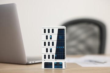 Real estate. Apartment building model, paperwork and laptop on wooden table indoors, closeup