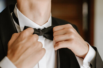 Close-up of man tying elegant bow tie to white shirt collar, detail of hands adjusting formal accessory