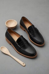 Elegant composition of black leather loafers with wooden spoon and small bowl on gray minimalist background, showcasing premium craftsmanship, modern masculine style, and luxury product design aesthet