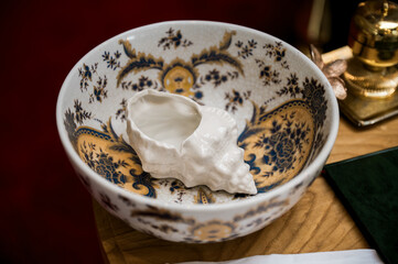 Close-up of ornate porcelain bowl with seashell-shaped vessel, symbolizing baptism, tradition, and elegance in Christian religious ceremonies.
