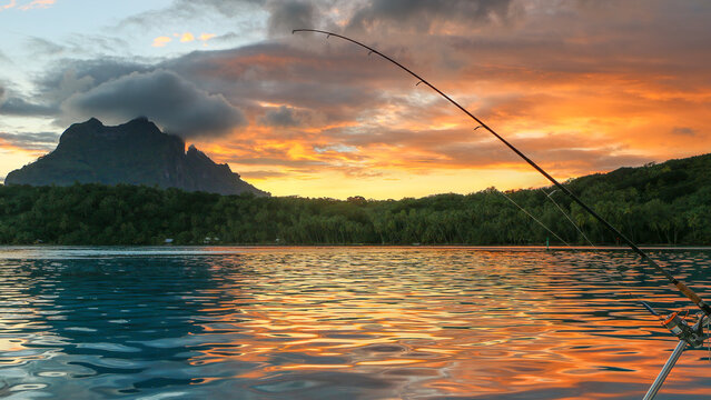 Lone fishing rod waiting for bites while at anchor during a gorgeous orange cloud sunset from a South Pacific lagoon in Bora Bora, Tahiti.