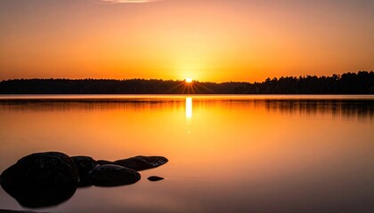 Scenic Golden Sunset Over Calm Water Reflecting The Horizon and Silhouette Trees With Rocks In Foreground