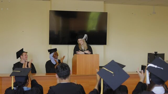 A young woman stands at the lectern and delivers a graduation speech to her classmates. 
