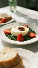 A plate of fresh goat cheese with strawberries, pecans, and greens served with bread on a sunlit table.