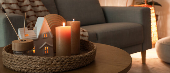 Tray with burning candles and reed diffuser on table in living room at night, closeup