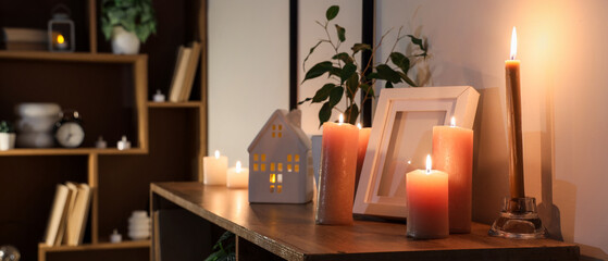 Burning candles with frame on shelf in room at night