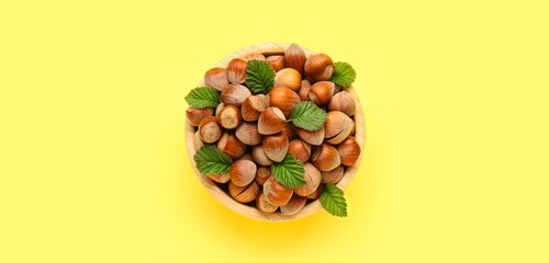 Bowl of tasty hazelnuts on yellow background, top view