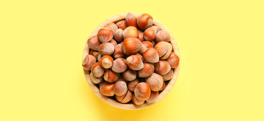 Bowl with shelled hazelnuts on yellow background