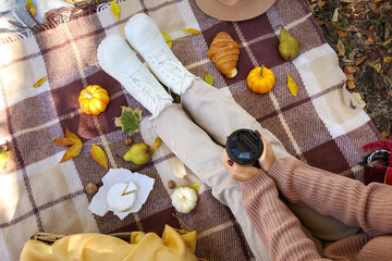 Young woman with cup of coffee and tasty food sitting on picnic in autumn park, top view