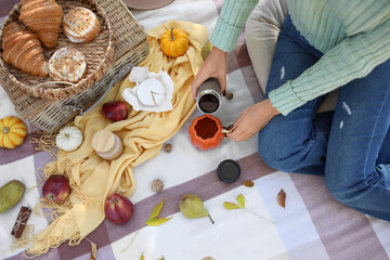 Young woman with tasty food pouring tea into cup on picnic in autumn park, top view