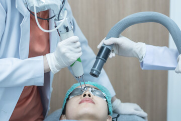 Asian woman wearing protection glasses getting laser skin face treatment.