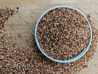 Raw buckwheat in a white bowl on wooden surface. Top view