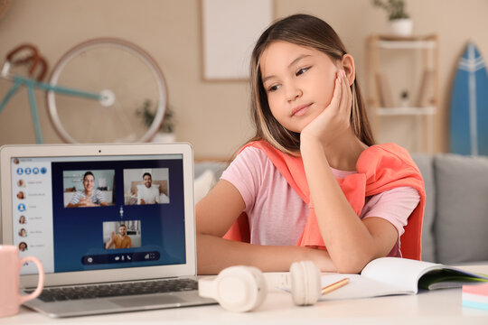 Happy teenage Asian girl with laptop sitting on online lesson at home