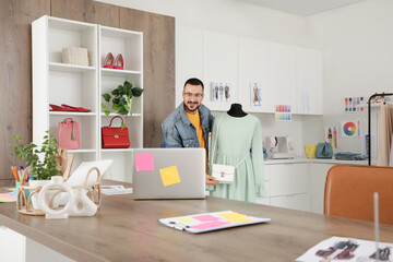 Happy male stylist with laptop video chatting and showing dress in studio