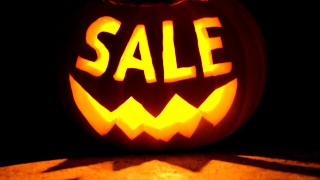 Carved pumpkin illuminated from within, displaying the word "SALE" and a jagged grin