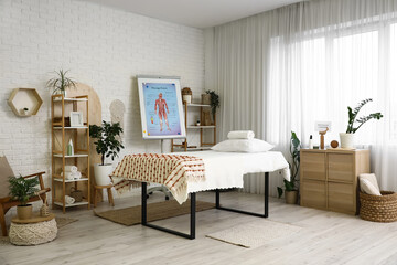 Interior of massage therapist's office with couch, shelving units and poster on flipchart in modern medical centre