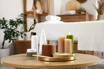 Cosmetic products with candles on table near massage therapist's couch in modern medical centre