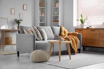 Interior of stylish living room with grey sofa, shelving units and coffee table