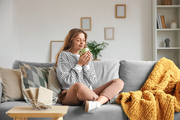 Beautiful young happy woman with cup of tea sitting on sofa at home