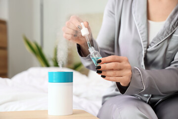 Young woman with essential oil and air humidifier in bedroom, closeup