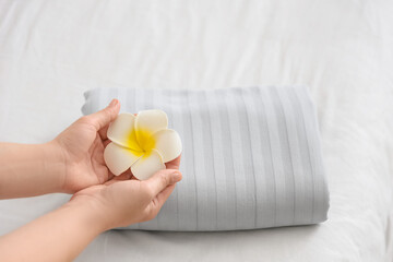 Female hands with clean bedsheet and plumeria flower on bed in hotel room, top view