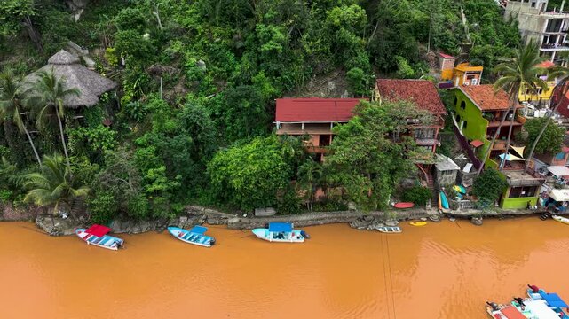 Casas en la orilla de un mar cafe y peque&ntilde;os barcos enfrente de las casas rodeado de selva, toma aerea con dron