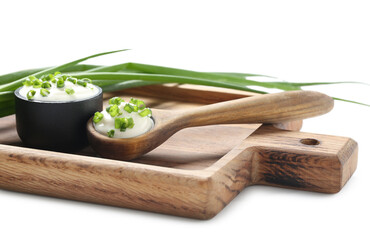 Cutting board with bowl and spoon of tasty sour cream and chopped green onion on white background