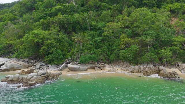 Toma aerea de zoom in a la playa Madagascar al sur de boca de tomatlan cerca de puerto vallarta jaslisco, olas tranquilas golpean la arena blanca, piedras gigantes enterradas en la arena y selva