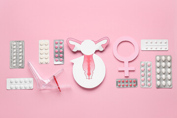 Gynecological speculum with symbol of woman, paper uterus and many different pills on pink background