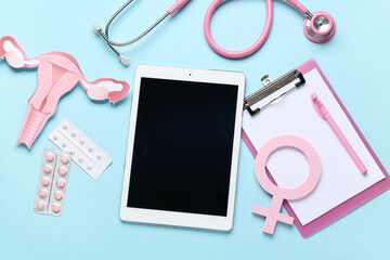 Tablet with clipboard, paper uterus, symbol of woman, stethoscope and pills on blue background