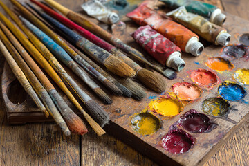Fototapeta premium Paintbrushes with colorful paint palette and tubes on wooden table