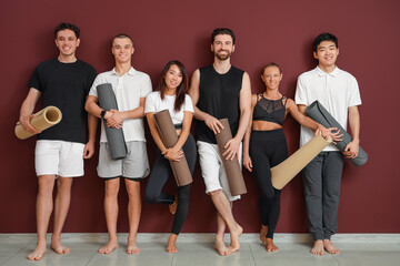 Obraz premium Group of sporty young people with yoga mats near red wall
