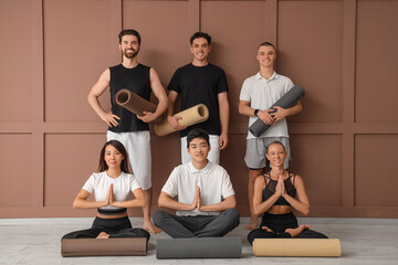 Group of sporty young people with yoga mats near brown wall