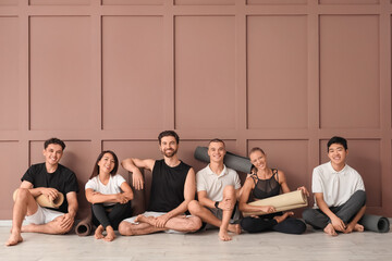 Fototapeta premium Group of sporty young people with yoga mats sitting near brown wall