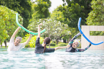 Trainer with Senior Couple Exercising in a Swimming Pool, Happy Elderly Asian People Doing Aqua Aerobics with Pool Noodles, Active Retirement, Cheerful Senior Couple Enjoys Water Exercise