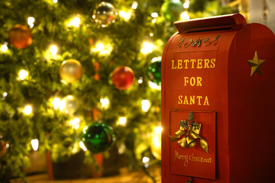 Christmas mailbox for mailing letters to Santa Claus. Closeup. Defocused Christmas tree with lights and ornaments in the background.
