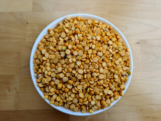 Yellow dry peas in the white bowl and on the wooden table