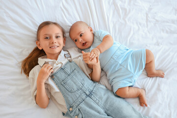 Little girl with her baby brother lying on bed, top view