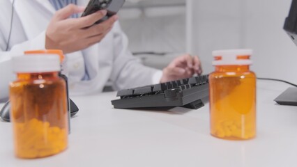 Close-up, male Asian doctor's hand typing computer keyboard and chats online message from mobile phone, pharmacy prescribes medicines by remote telemedicine technology, and hospital call center.