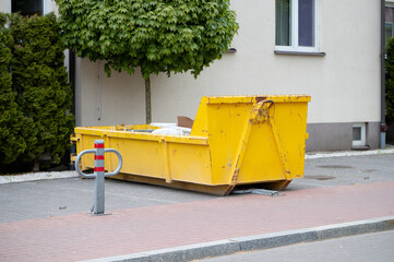 Large yellow container for construction waste near apartment building during renovation. Used for temporary storage of debris during construction and demolition.