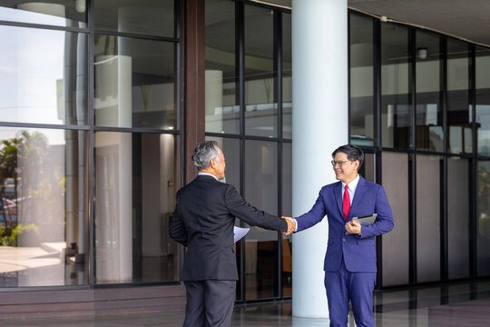 Generations of business professionals celebrating success. An older and younger man in suits have handshake, symbolizing achievement, teamwork, agreement, and work relationships.