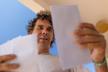 A view from below of a young man reading a letter while standing near a mailbox.