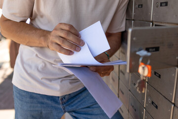 A young man reads a letter while standing at a mailbox.