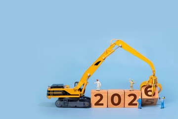 Transitioning from 2025 to 2026 with wooden blocks and miniature excavator. new year 2026 concept with blue background.