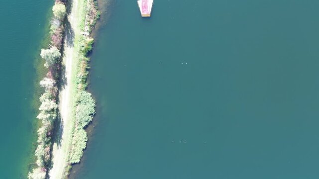 Aerial downward view of a dike dividing the lake. Trees line a dirt road on the dike. A water ski slalom course with ramp and buoys is clearly visible.